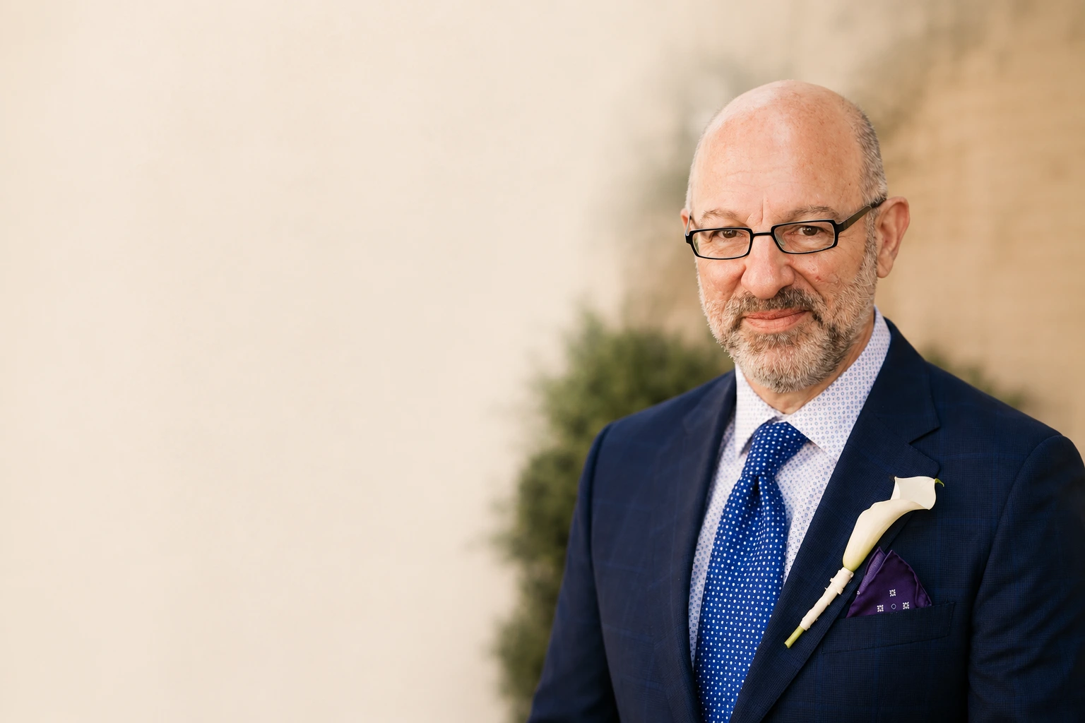 Andrew Akers in a suit standing against a soft architectural background